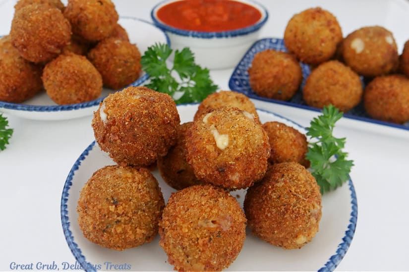 A white surface with three plates with deep fried Italian sausage bites on them.