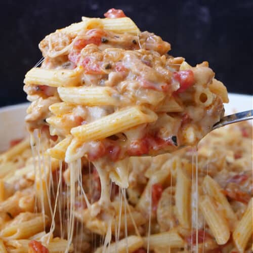 A serving spoon scooping out a big spoonful of cheesy pasta with sausage.