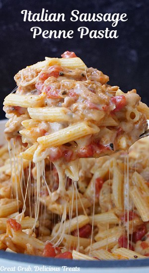 A big spoonful of cheesy pasta and sausage being scooped out on the pan showing all the stretchy cheese.