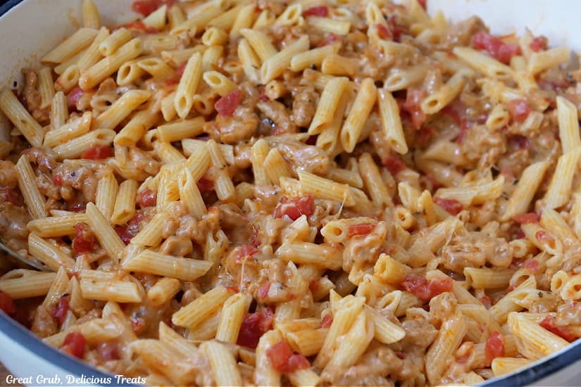 A white cast iron skillet filled with sausage, cheese, and pasta.