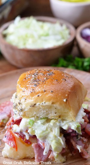 An Italian slider on a small wood plate with a wood bowl filled with shredded lettuce in the background.
