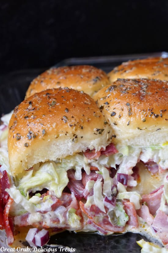 A close up of a few sliders with meat, a lettuce mixture on Hawaiian rolls topped with seasoned melted butter.