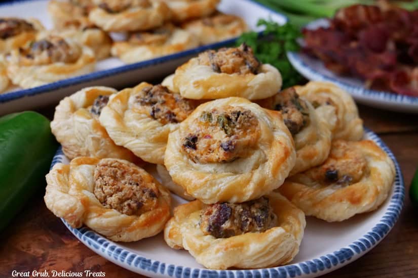 A horizontal photo of white plates with blue trim with mini bite-size purr pastries that are filled with jalapeno popper mixture.