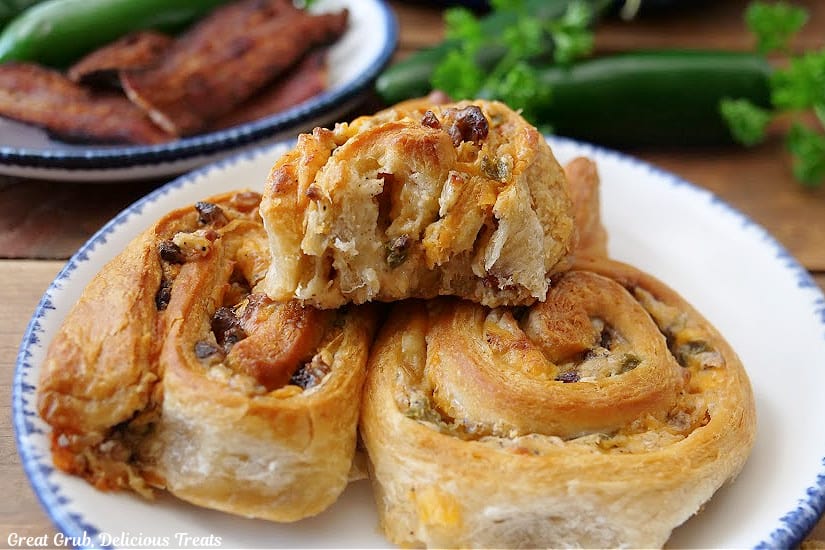A horizontal photo of a small white round plate with blue trim with three jalapeno popper pinwheels on it.