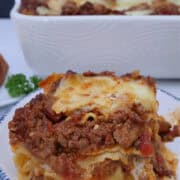 A round white plate with blue trim with a serving of lasagna bolognese on it.