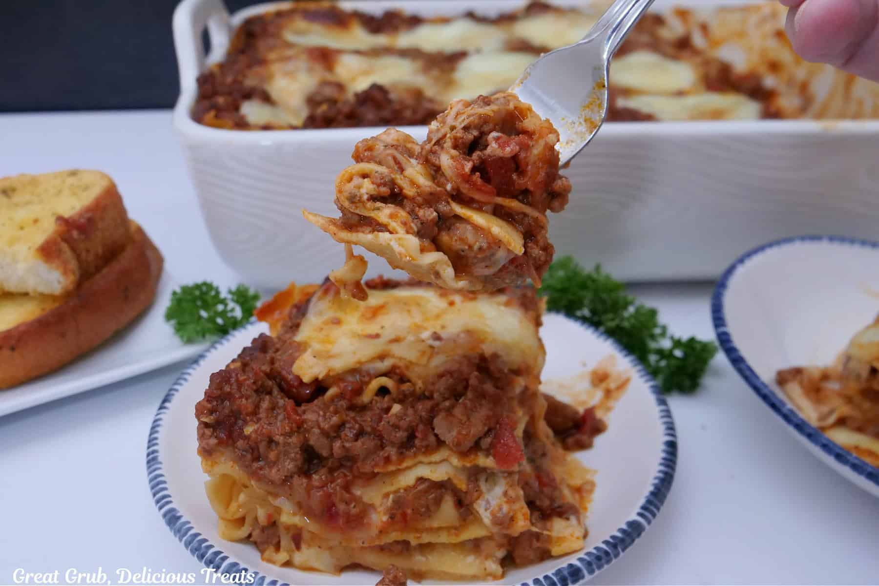 A white surface with a serving of lasagna on three plates with the baking dish in the background.