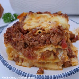 A serving of lasagna bolognese on a white plate with blue trim.