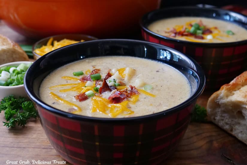 A wood surface with two red and black plaid bowls with potato soup in them.