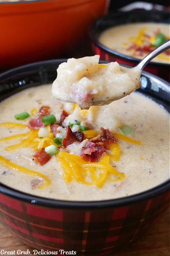 A red and black plaid bowl filled with potato soup and a spoonful of soup held above the bowl.