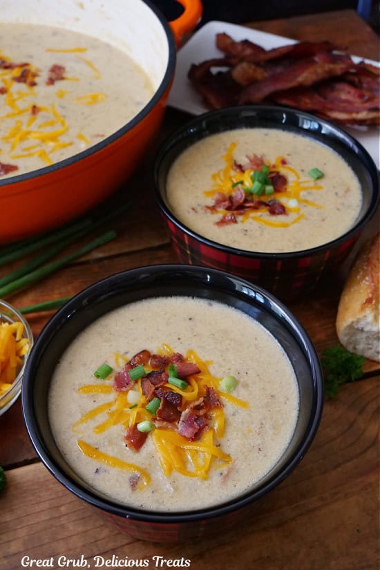 A wood surface with tow plaid bowls filled with potato soup and the orange pot the soup was made in in the background.