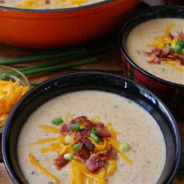 Two red and black plaid bowls filled with a serving of potato soup with a orange pot in the background.