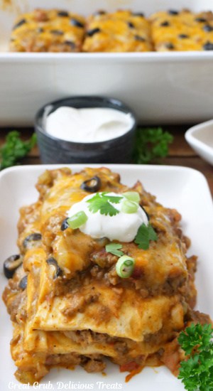 A white plate with a serving of Mexican Lasagna with the baking dish in the background.