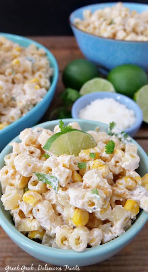 Mexican Street Corn Pasta Salad is a great side dish to make that pairs perfectly with your favorite Mexican dish. A small bowl filled with Mexican street corn pasta salad, a small bowl of cojita cheese, and limes in the background.