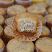 Mini banana muffins place on a hard surface with a bite taken out of one of the muffins on top.