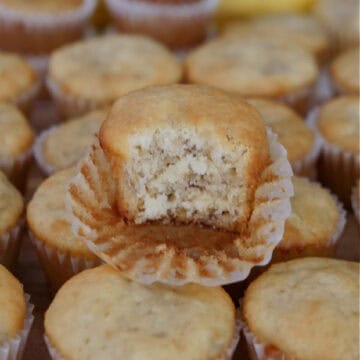 Mini banana muffins place on a hard surface with a bite taken out of one of the muffins on top.