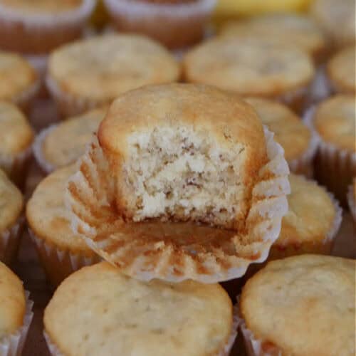 Bite size banana muffins place on a hard surface with a bite taken out of one of the muffins on top.