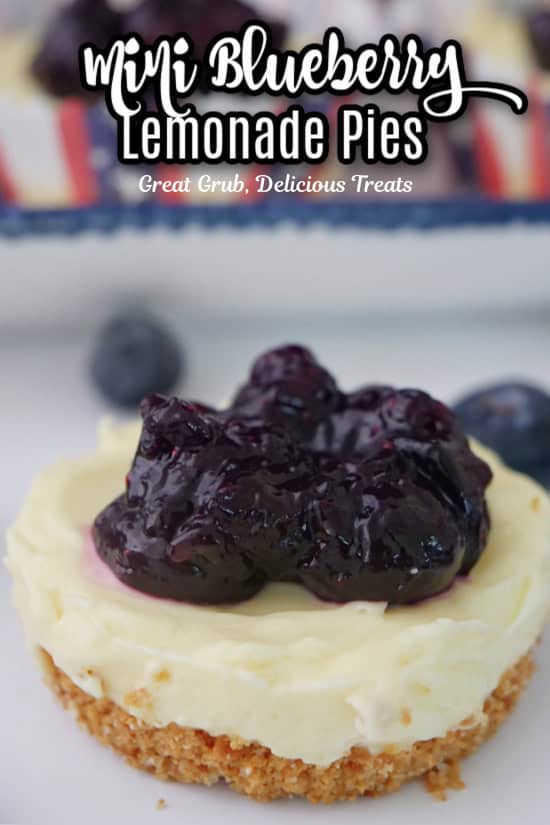 A white surface with a mini blueberry lemonade pie on it with more mini pies in the background.