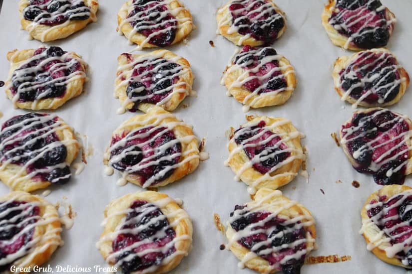 A baking sheet with 16 mini blueberry pastries on it.