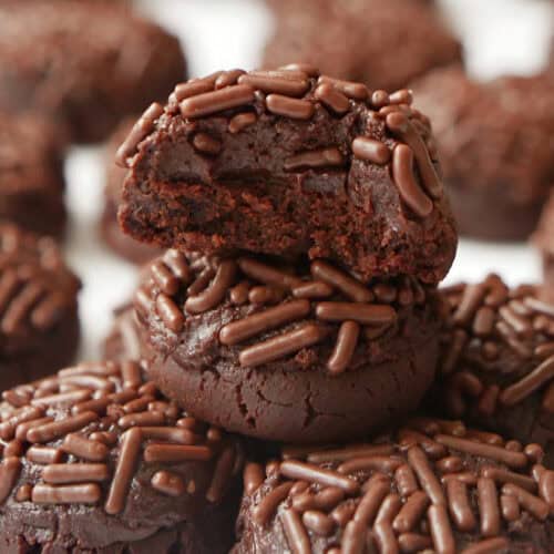 A white surface with mini brownie bites stacked on each other with a bite taken out of the top mini brownie.