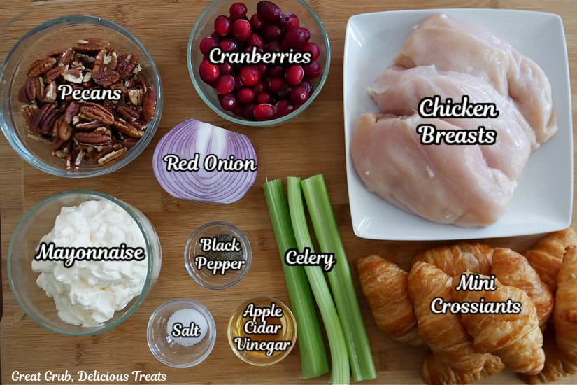 A wood surface with all the ingredients needed to make chicken cranberry salad with mini croissants.