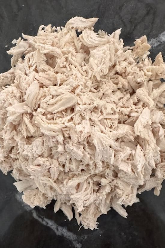 A glass bowl filled with shredded chicken.