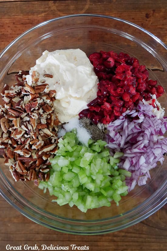 A wood surface with a glass bowl filled with all the ingredients for chicken cranberry salad.