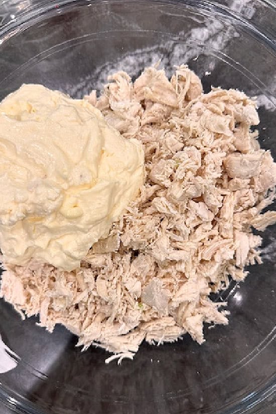 A glass bowl filled with shredded chicken and mayonnaise.