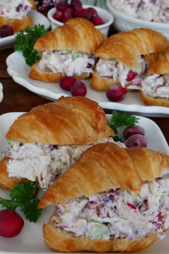 A few white plates with mini chicken cranberry salad croissants on them.