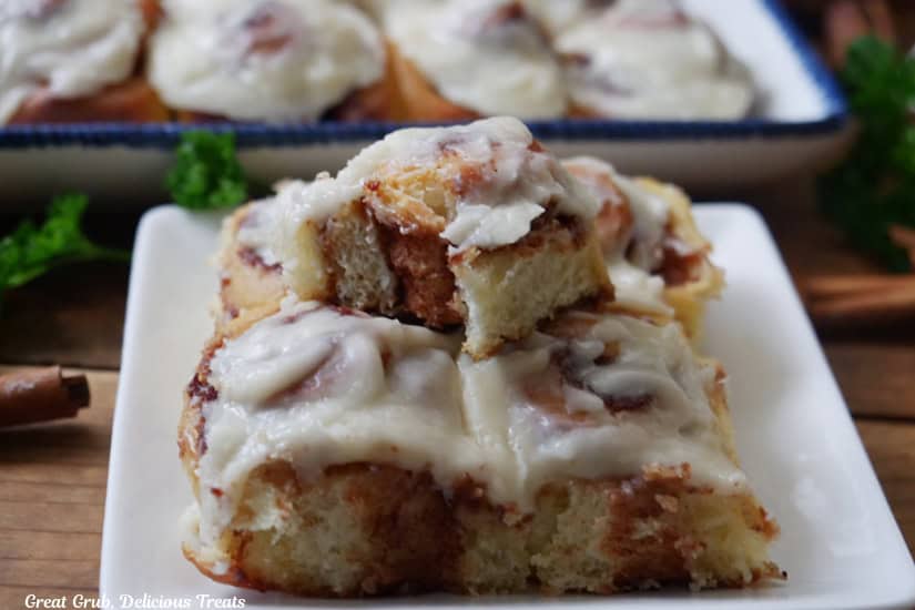 A white square plate with 5 mini cinnamon rolls on it and the one on top has a bite taken out of it.