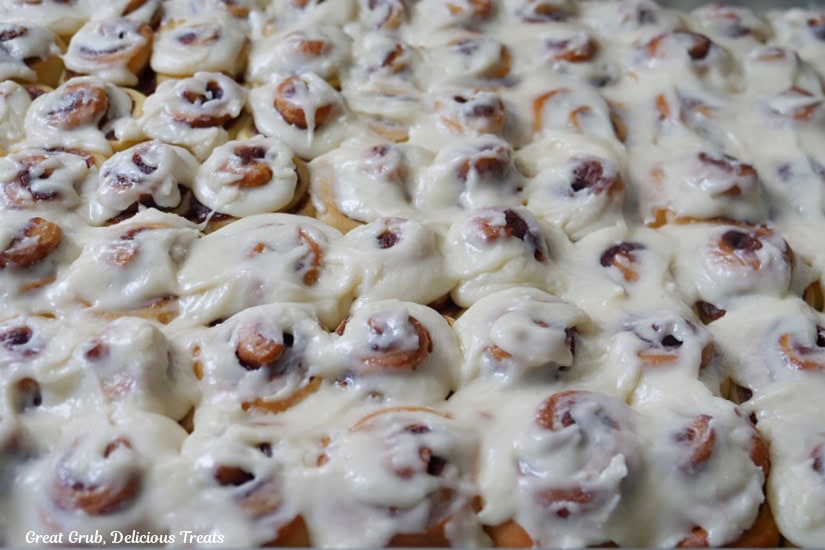 A large baking sheet with approximately 50 iced mini cinnamon rolls on it.