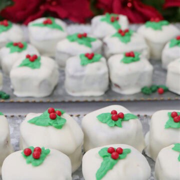 Two sliver trays with mini gingerbread bites covered in white chocolate and green and red decorations on top of each one.