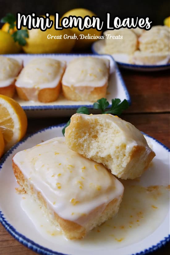 A small round white plate with blue trim with two mini lemon loaves on it with a bite taken out of one of them.