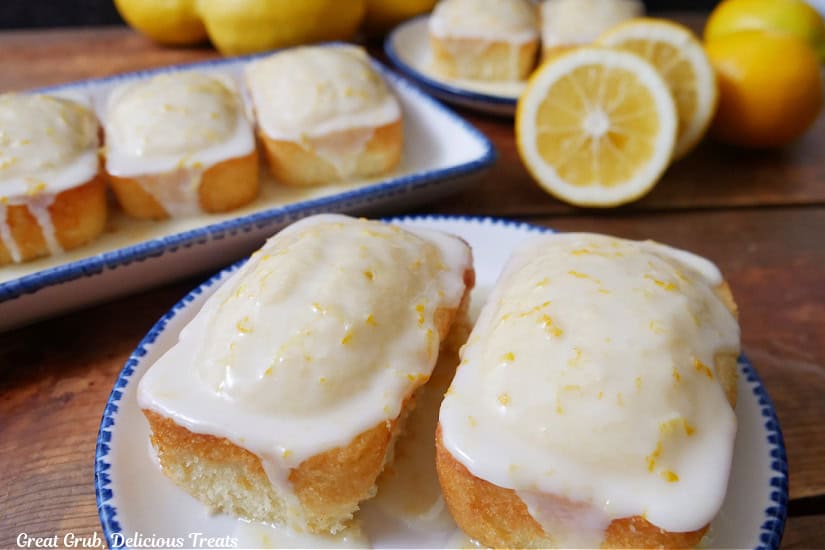 Three white plates with blue trim with mini lemon loaves on them with fresh lemons in the background.