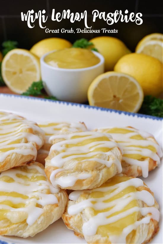 A white plate with blue trim with 6 mini lemon pastries on it with lemons in the background.