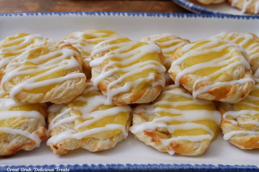 A horizontal photo of a white oblong plate with blue trim with eleven mini lemon pastries on it.