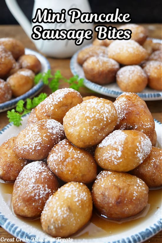 Three white plates with blue trim filled with mini pancake sausage bites with powdered sugar and syrup on them.