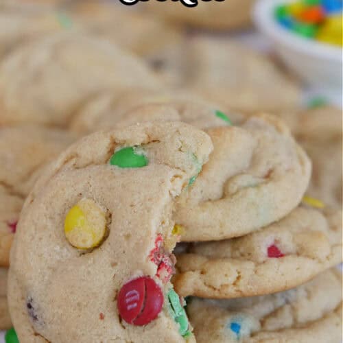 A white surface with mini peanut butter cookies placed on the surface with a few stacks of cookies and one with a bite taken out of it.