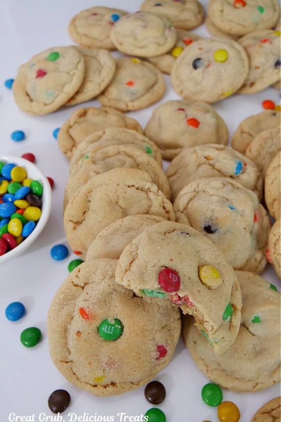A white surface with about three dozen bite-size cookies on it with mini M&Ms scattered around.