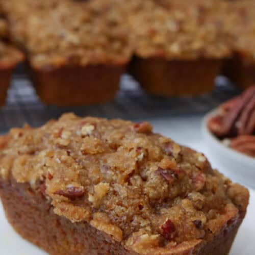 A white square plate with a mini pumpkin loave on it with more mini loaves in the background.
