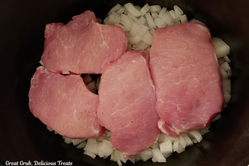 Pork chops, onions, and garlic in a black crock pot insert.