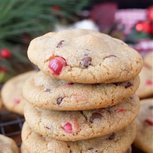A stack of five M&M chocolate chip cookies on a wire rack with more cookies on the rack.