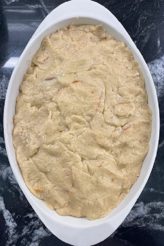 A black surface with a white oval baking dish with the cobbler topping covering the nectarine filling.