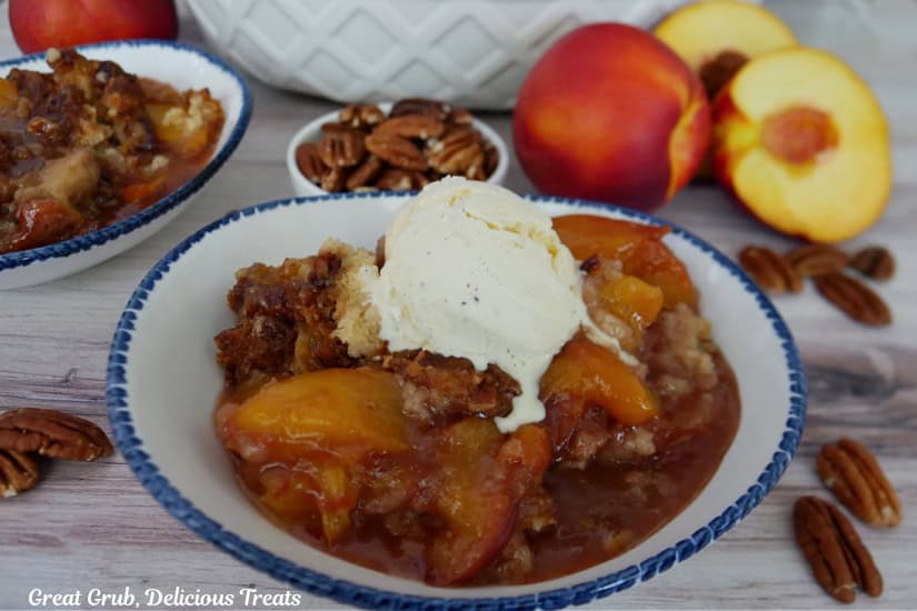 A white surface with a white bowl with blue trim filled with a serving of nectarine cobbler with a scoop of vanilla ice cream on top.
