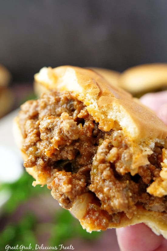 A sloppy joe, held up above another sloppy joe, with a few bites taken out of it.