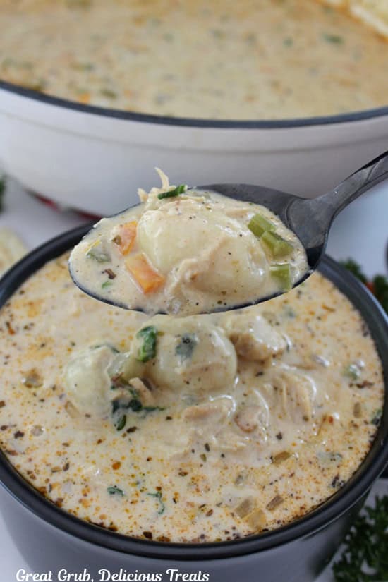 A black soup bowl filled with chicken gnocchi soup and a spoonful being scooped out and held above the bowl.