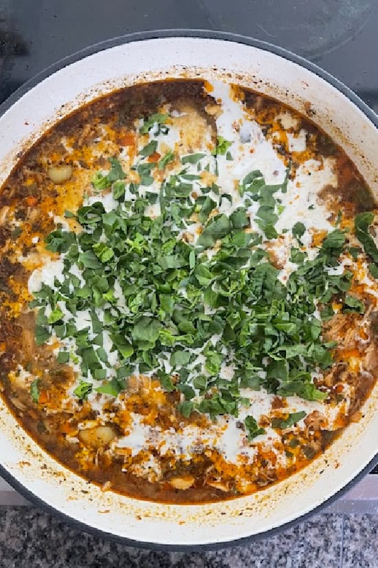 A white pot with all the ingredients in it to make chicken gnocchi soup.