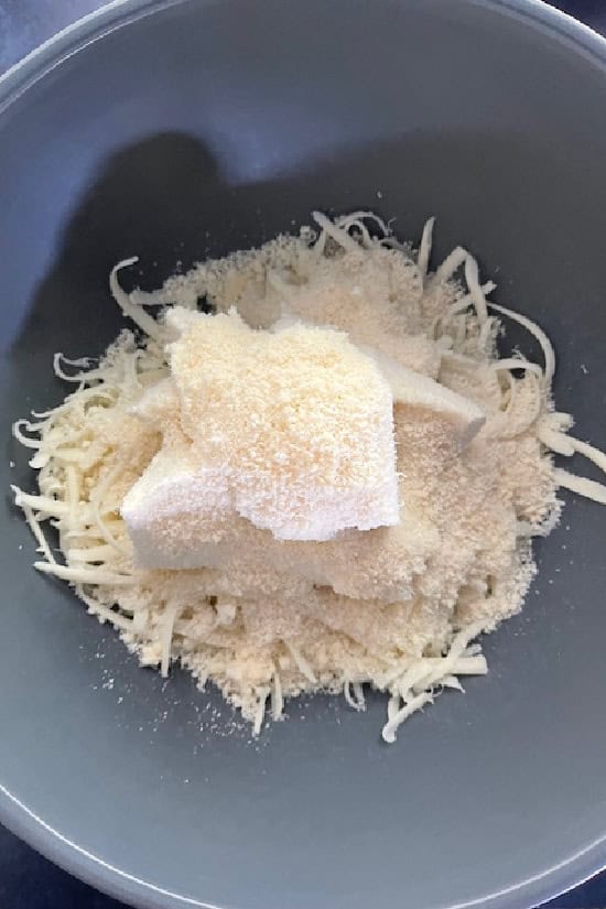 Shredded mozzarella cheese, parmesan cheese, and ricotta cheese in a light blue bowl.