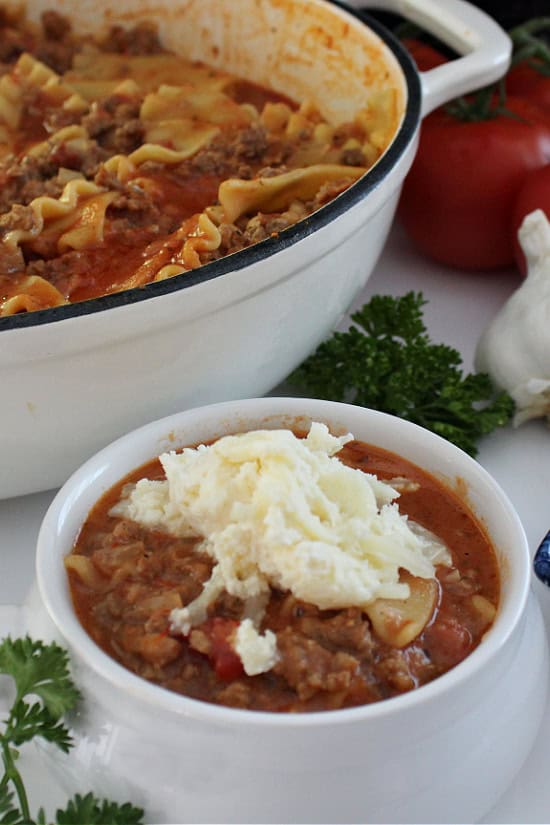 A white soup bowl with lasagna soup in it topped with a cheese mixture on it.