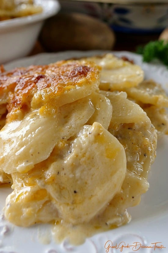 Cheesy Garlic Scalloped Potatoes are super rich, cheesy and incredibly delicious A serving of Cheesy Garlic Scalloped Potatoes on a white plate.