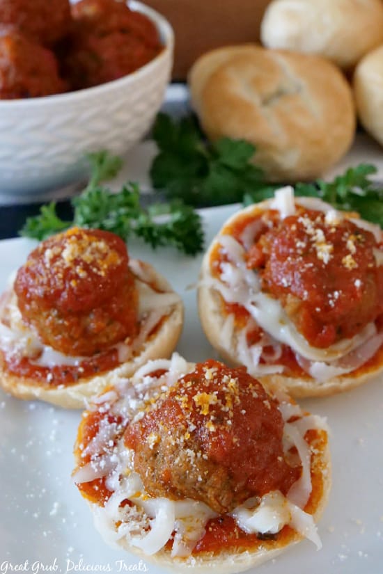 Meatball Bagel Bites are easy to make, delicious, and sure to be enjoyed by the entire family. Meatball Bagel Bites on a white plate with parsley, meatballs in a white bowl, and plain bagels in the background.